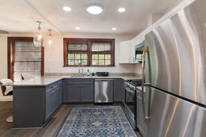 A modern kitchen with a stainless steel refrigerator, built-in dishwasher, and a granite countertop. - The Gainesville Rock House (Gainesville)