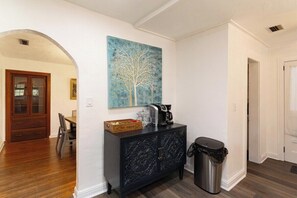 A hallway with a dark wooden cabinet, a trash can, and a painting of a tree. - The Gainesville Rock House (Gainesville)