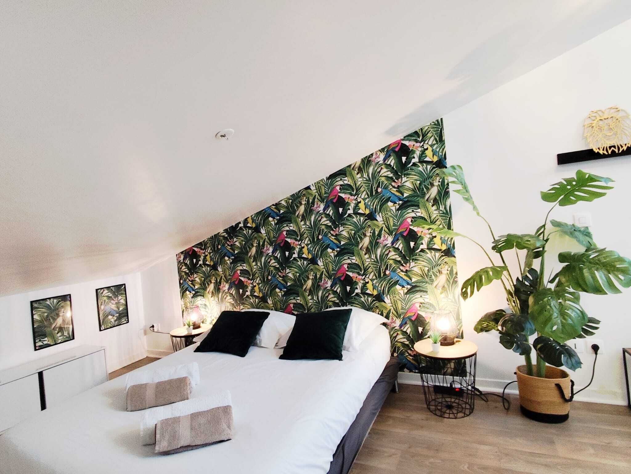 A bedroom with a bed, a nightstand, a lamp, and a large potted plant.