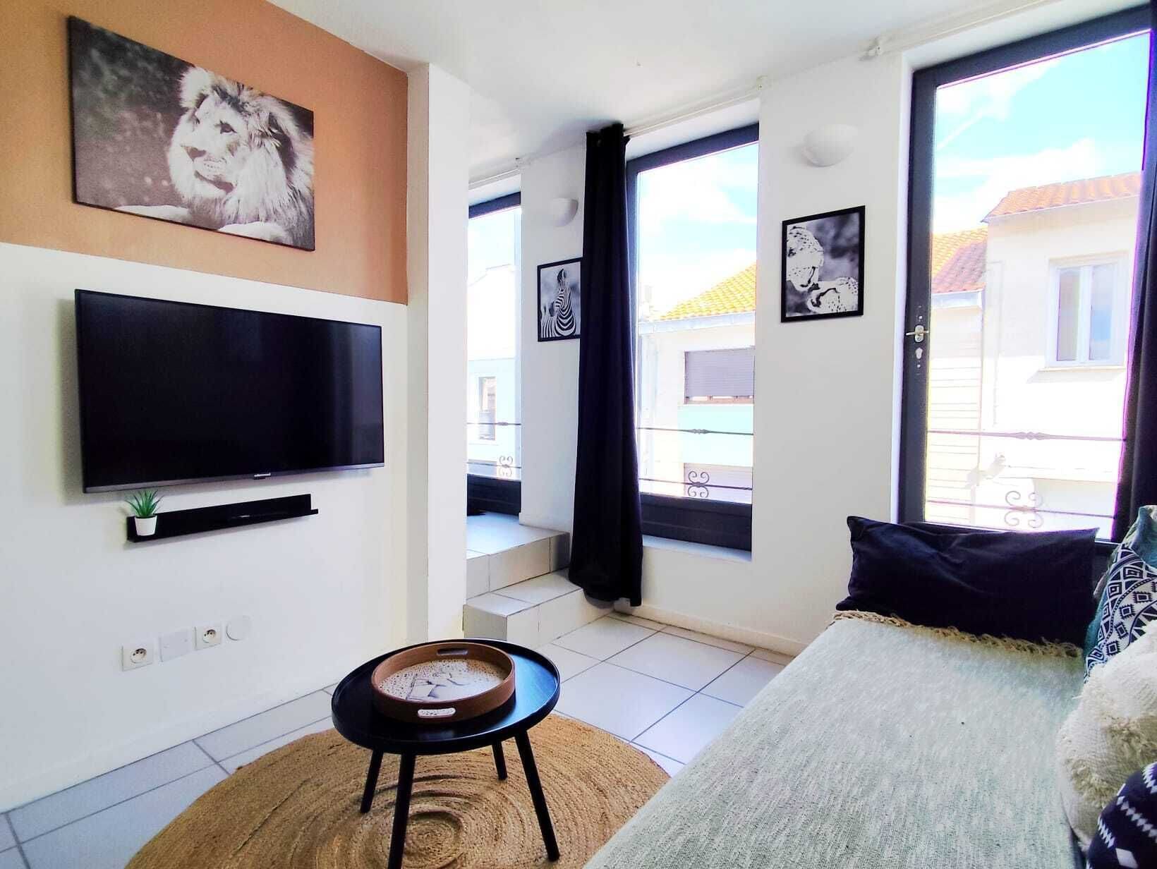 A living room with a flat-screen TV, a small table, a sofa, and a window with a view of buildings.