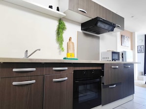 Eine moderne Küche mit dunklen Holzschränken, einem eingebauten Backofen, einer Mikrowelle und einer schwarzen Dunstabzugshaube.