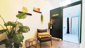 Et værelse med trægulv, en rund vævet måtte, en stol med et mønstret sædehynde, en potteplante, et lille firkantet bord og en døråbning til et badeværelse.