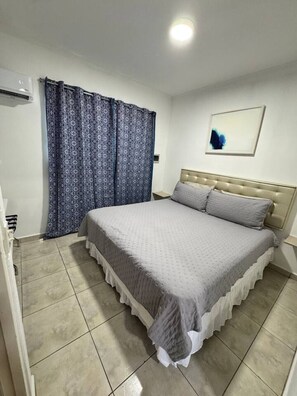 Ein Schlafzimmer mit einem Bett, Vorhängen, einer Wandlampe und einem gerahmten Bild.