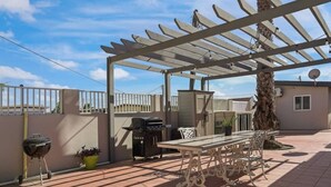 Eine Terrassengruppe im Freien mit Pergola, Grill, Tisch und Stühlen sowie einem Blumentopf.