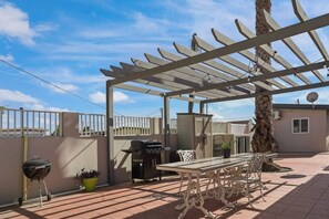 Eine Terrassengruppe im Freien mit Pergola, Grill, Tisch und Stühlen sowie einem Blumentopf.