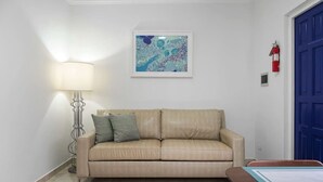 Ein beiges Ledersofa mit zwei Kissen, eine Stehlampe, ein gerahmtes abstraktes Gemälde, eine blaue Tür und ein Feuerlöscher an der Wand.