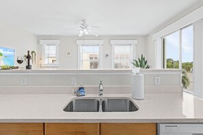 A modern kitchen with a large island, a double sink, and a ceiling fan.
