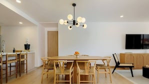 Ein moderner Essbereich mit einem Holztisch und Stühlen, einer Kristallleuchtre und einem an der Wand befestigten Fernseher.