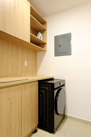 A laundry area with a washing machine, wooden cabinets, and a utility panel. - Homey 3BR Apt near Parque México|Pool & Gym (Ciudad de México)