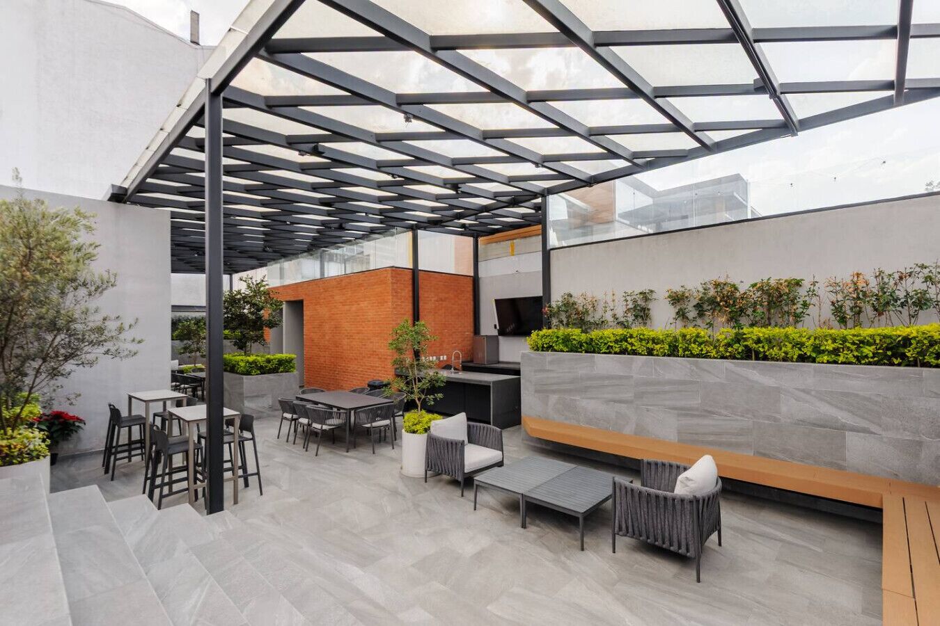 An outdoor patio with a glass ceiling, seating arrangements, and a brick wall with greenery.