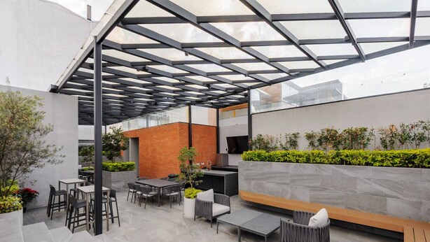 Eine Terrasse im Freien mit Glasdach, Sitzgelegenheiten und einer Ziegelwand mit Bepflanzung.