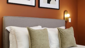 Ein Hotelzimmer mit einem Bett, Kissen, einem Nachttisch und zwei gerahmten Bildern an der Wand.