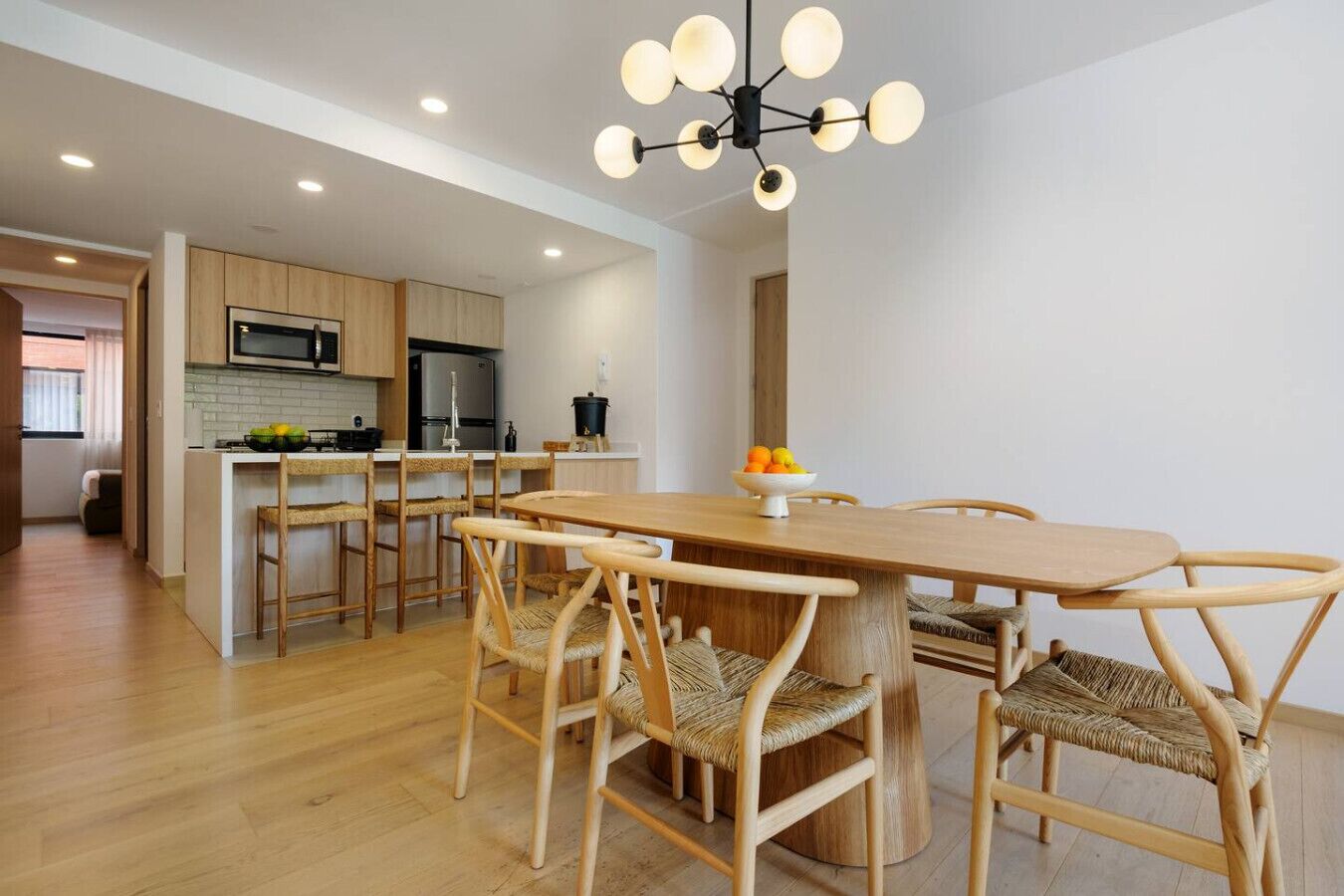 Une cuisine moderne avec des meubles en bois, un îlot central et un coin repas comprenant une table ronde et des chaises en osier.