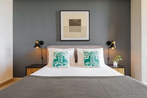A neatly made bed with a grey textured bedspread, two pillows with green floral designs, and a framed abstract artwork above the bed. - ¡NEW! Modern apt. with Bellas Artes views (Ciudad de México)