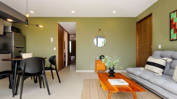 Ein modernes Wohnzimmer mit Sofa, Couchtisch und Sesseln. Es gibt einen Essbereich mit Tisch und Stühlen. Im Hintergrund ist eine Küche erkennbar.