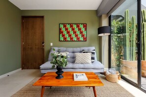 A living room with a sofa, a coffee table, a plant, a painting, and a cactus in a glass container. - ¡NEW! Modern apt. with Bellas Artes views (Ciudad de México)