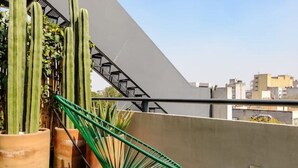 Eine Dachterrasse mit einem grünen Stuhl, zwei kleinen Tischen und Kakteen in Töpfen.