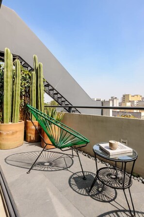 Eine Dachterrasse mit einem grünen Stuhl, zwei kleinen Tischen und Kakteen in Töpfen.
