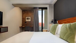 A hotel room with a large bed, a desk, a chair, a television, and a view through a glass door. - Modern & Bright Apt. Steps from Revolución (Ciudad de México)