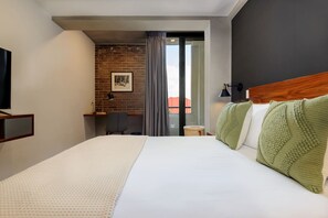 Quarto de hotel com uma cama grande, uma escrivaninha, uma cadeira, uma televisão e vista através de uma porta de vidro.