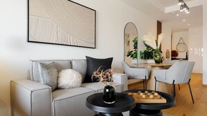 Una sala de estar moderna con un sofá gris, una mesa de centro negra redonda y un comedor con una mesa y sillas de madera.