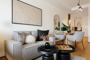 Ein modernes Wohnzimmer mit einem grauen Sofa, einem runden schwarzen Couchtisch und einem Essbereich mit einem Holztisch und Stühlen.