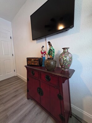 Ein Zimmer mit einem flachbildfernseher an der Wand, einer Holzkassette mit Schubladen und einer dekorativen Vase.
