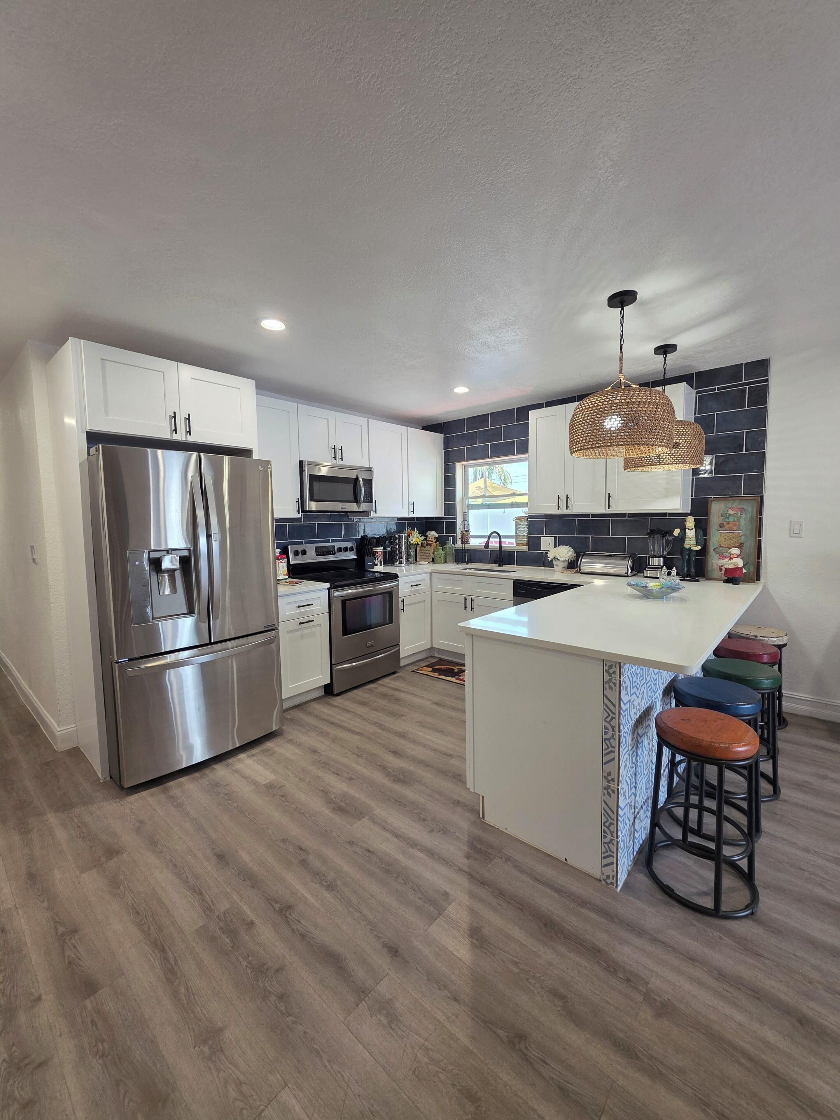 Una cocina moderna con electrodomésticos de acero inoxidable, una isla central con taburetes y una lámpara colgante decorativa.