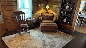 A wooden interior with a rocking chair, ottoman, and a shelf with decorative items. - Your Home Away From Home. Spacious 6-Bedroom Frewsburg Retreat room for everyone (Frewsburg)