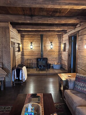 Ein gemütliches Blockhaushaus-Interieur mit Kaminofen, einer Couch und einem Esstisch.