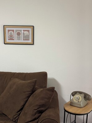 A brown sofa with cushions, a framed picture on the wall, and a vintage telephone on a small wooden table. - Mountain Getaway – House with a Panoramic View in the Seriana Valley (Rizzoli)