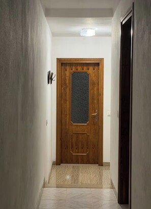 A hallway with a wooden door, a light fixture on the ceiling, and a tiled floor. - Mountain Getaway – House with a Panoramic View in the Seriana Valley (Rizzoli)
