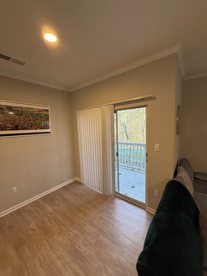 Una habitación con piso de madera, un ventanal corredero que da a un balcón y un cuadro en la pared.