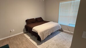 Ein Schlafzimmer mit einem Bett, einem Deckenventilator, einem Fenster mit Jalousien und einem grünen Sessel.