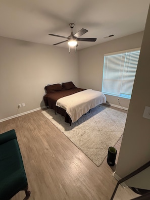 Un dormitorio con una cama, ventilador de techo, ventana con persianas y una silla verde.