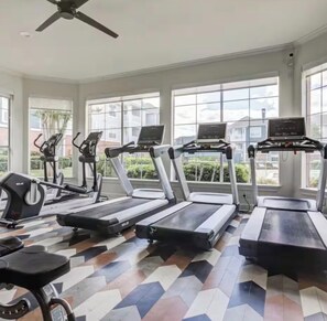 Un gimnasio con cintas de correr, elípticas y una bicicleta estática, amplias ventanas y piso estampado.