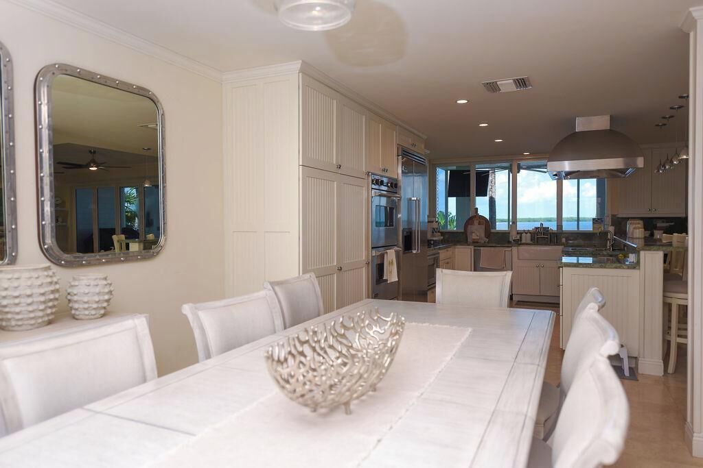 A modern kitchen with white cabinetry, a dining area with a white table and chairs, and a large window overlooking a body of water.