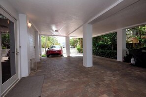 Ein überdachter Weg führt zu einer Garage, in der ein rotes Auto steht.