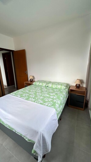 Un dormitorio con cama, mesita de noche, lámpara y una puerta.