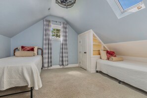 Ein Schlafzimmer mit zwei Einzelbetten, einem Fenster mit Vorhängen, einem Deckenventilator und einem Oberlicht.