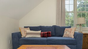 A blue sofa with patterned cushions, a wooden coffee table, and a window with a view of trees. - Luxury Retreat, Near Downtown Asheville, Pool, Dog-Friendly, 6BR/5BA, Spacious (Fletcher)