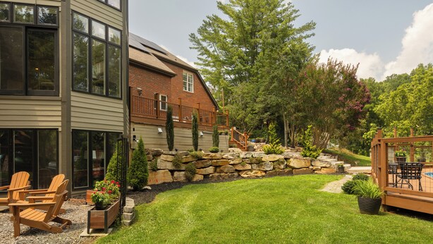 A modern house with a stone retaining wall, a grassy yard, and outdoor seating. - Luxury Retreat, Near Downtown Asheville, Pool, Dog-Friendly, 6BR/5BA, Spacious (Fletcher)
