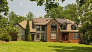A two-story house with a brick facade, a large front lawn, and a solar panel array on the roof. - Luxury Retreat, Near Downtown Asheville, Pool, Dog-Friendly, 6BR/5BA, Spacious (Fletcher)