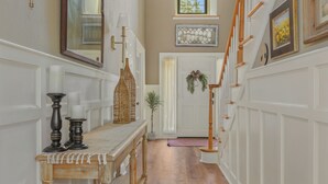 A hallway with a wooden bench, a mirror, and a door with a wreath. - Luxury Retreat, Near Downtown Asheville, Pool, Dog-Friendly, 6BR/5BA, Spacious (Fletcher)