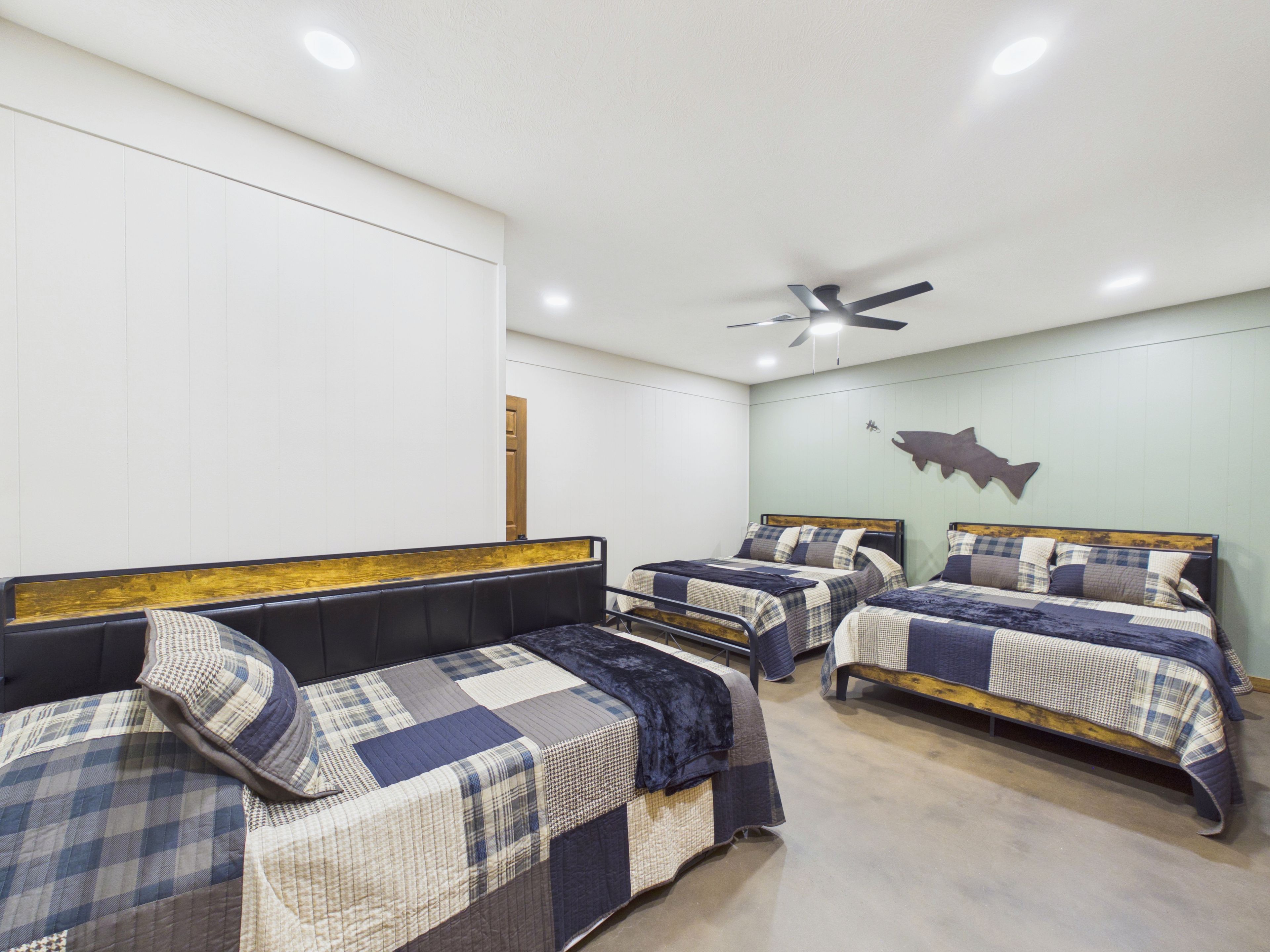 Een hotelkamer met drie bedden, een plafondventilator en een visdecoratie aan de muur.