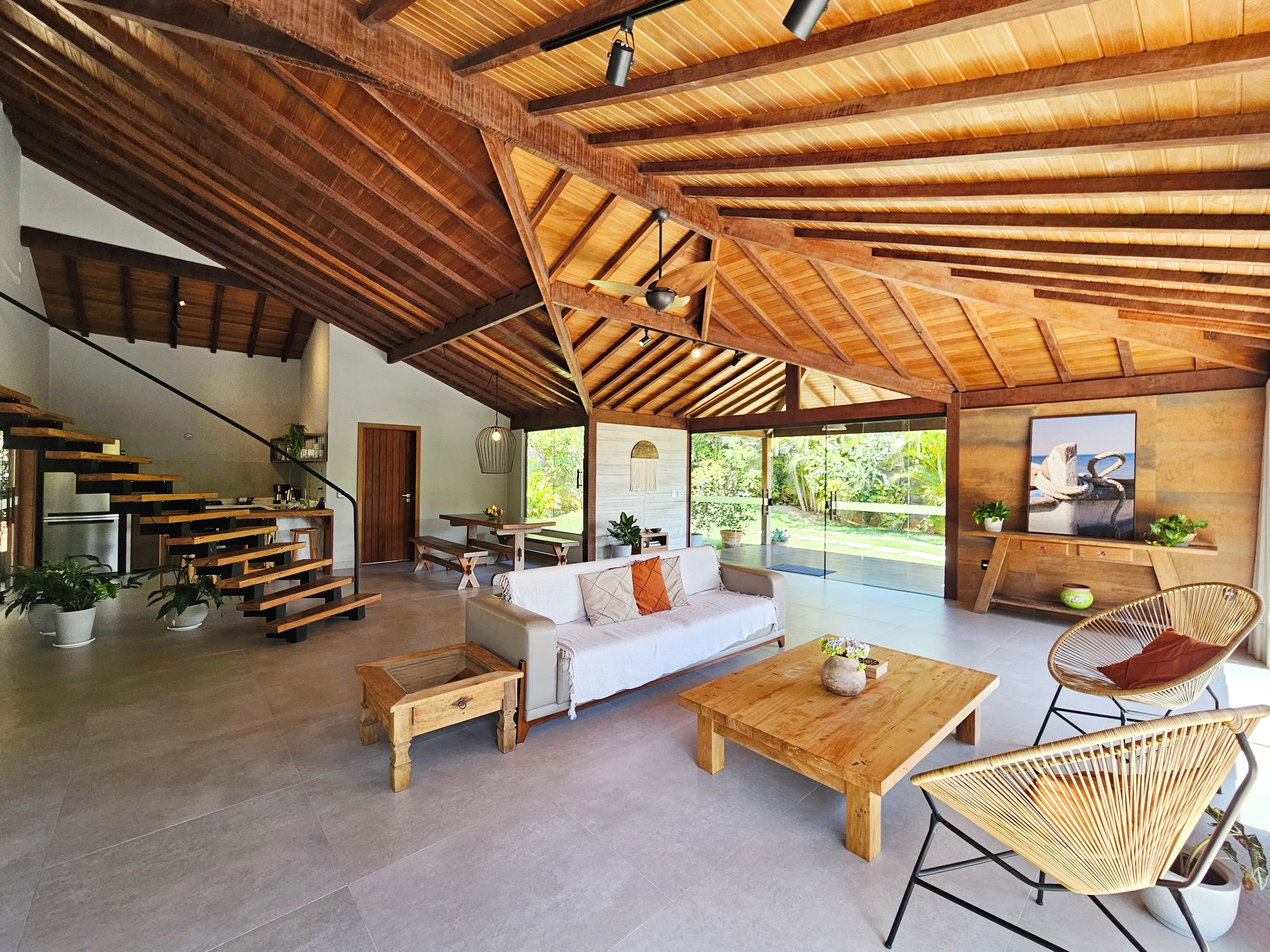 Un amplio salón con techo de madera, un sofá, una mesa de centro, sillas de mimbre y una escalera.