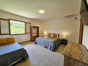 Ein Schlafzimmer mit zwei Betten, einem Holzschrank, einem Fernseher und einem Fenster mit Blick auf Grünflächen.
