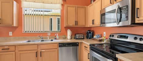 A modern kitchen with wooden cabinets, stainless steel appliances, and a window with blinds.