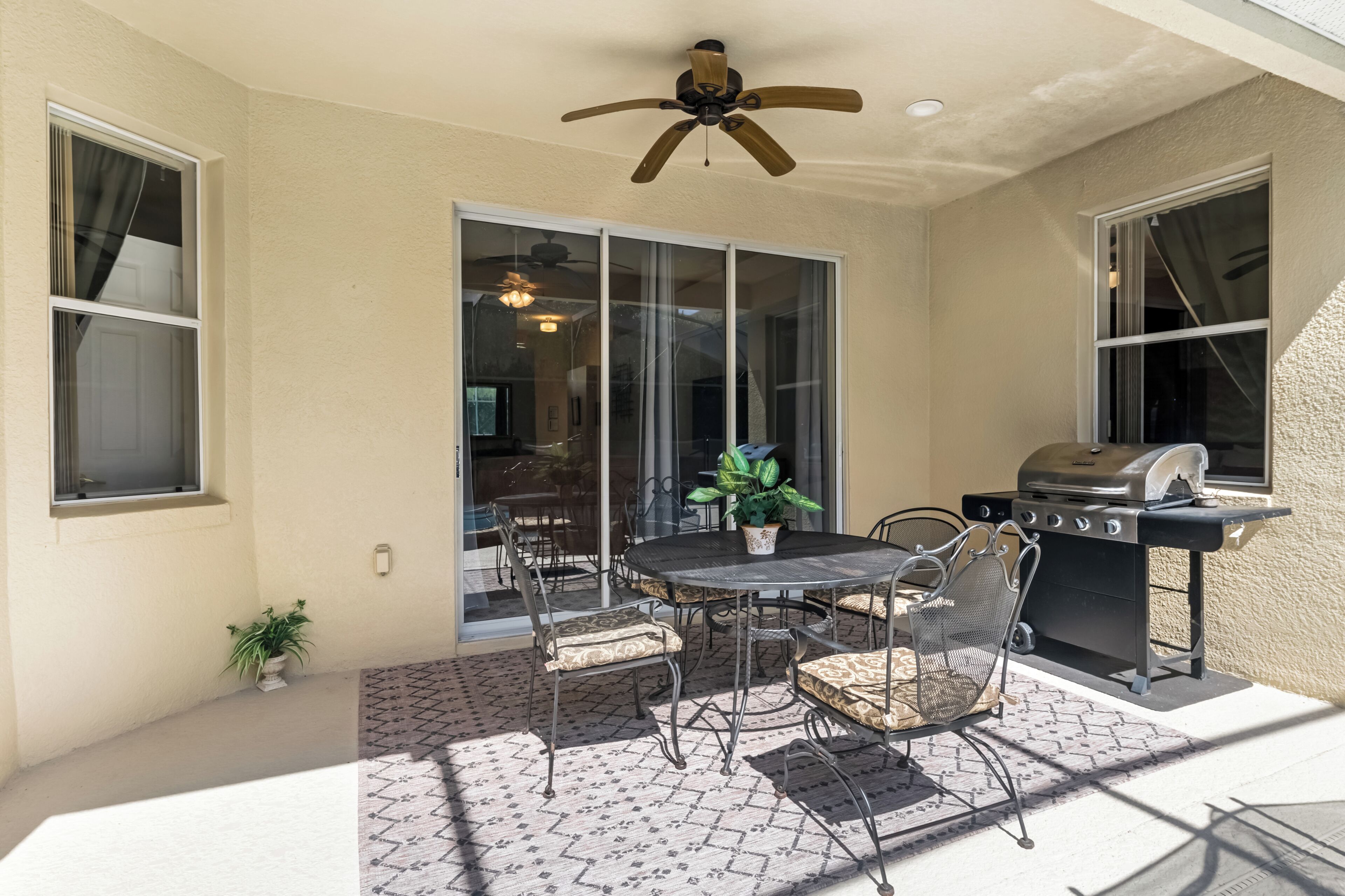 Une terrasse avec une table et des chaises, un ventilateur de plafond et un barbecue.