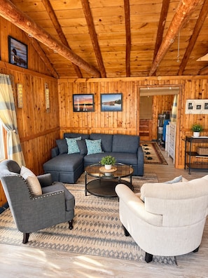 Un salon chaleureux avec un plafond en bois, un canapé bleu, deux fauteuils et une table basse.